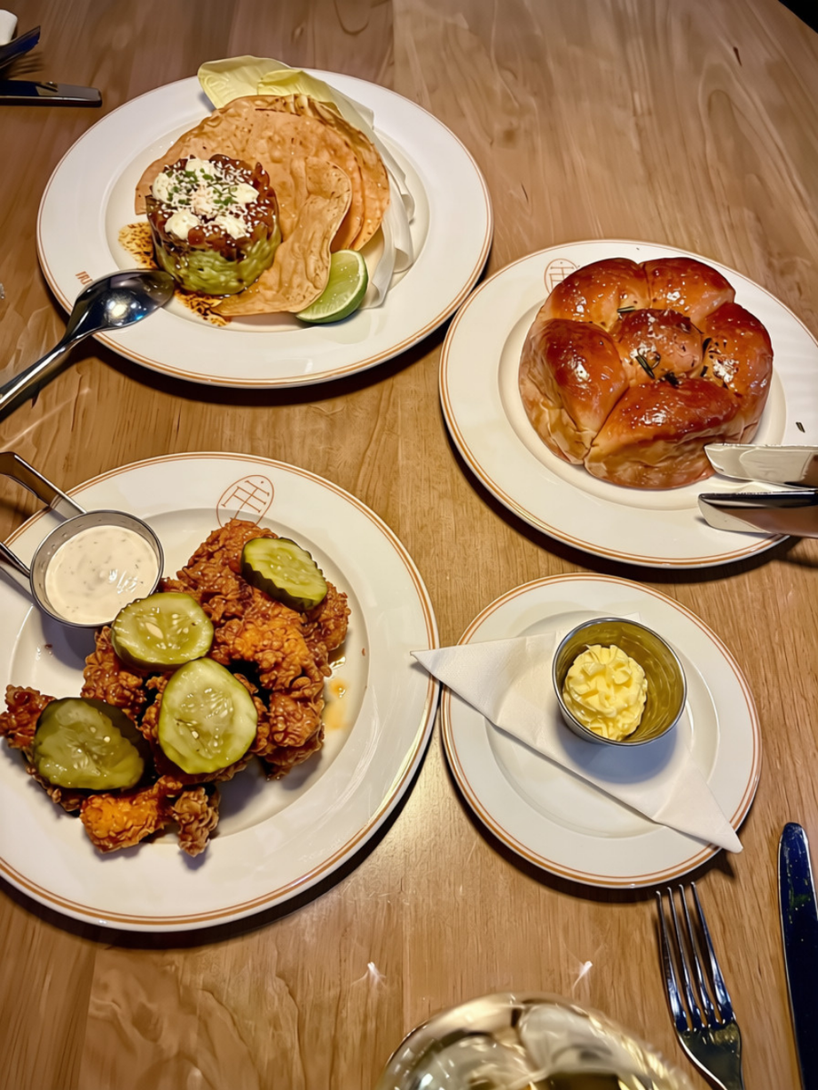 Overhead view of a shared meal with fried chicken, pickles, dinner rolls, and dips.