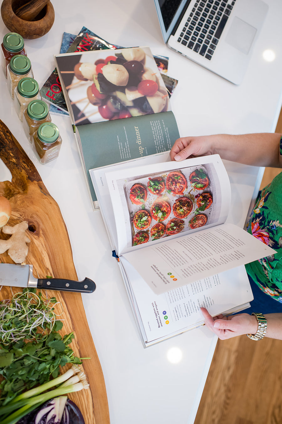 Hands flipping through a recipe book on a kitchen counter with fresh ingredients.